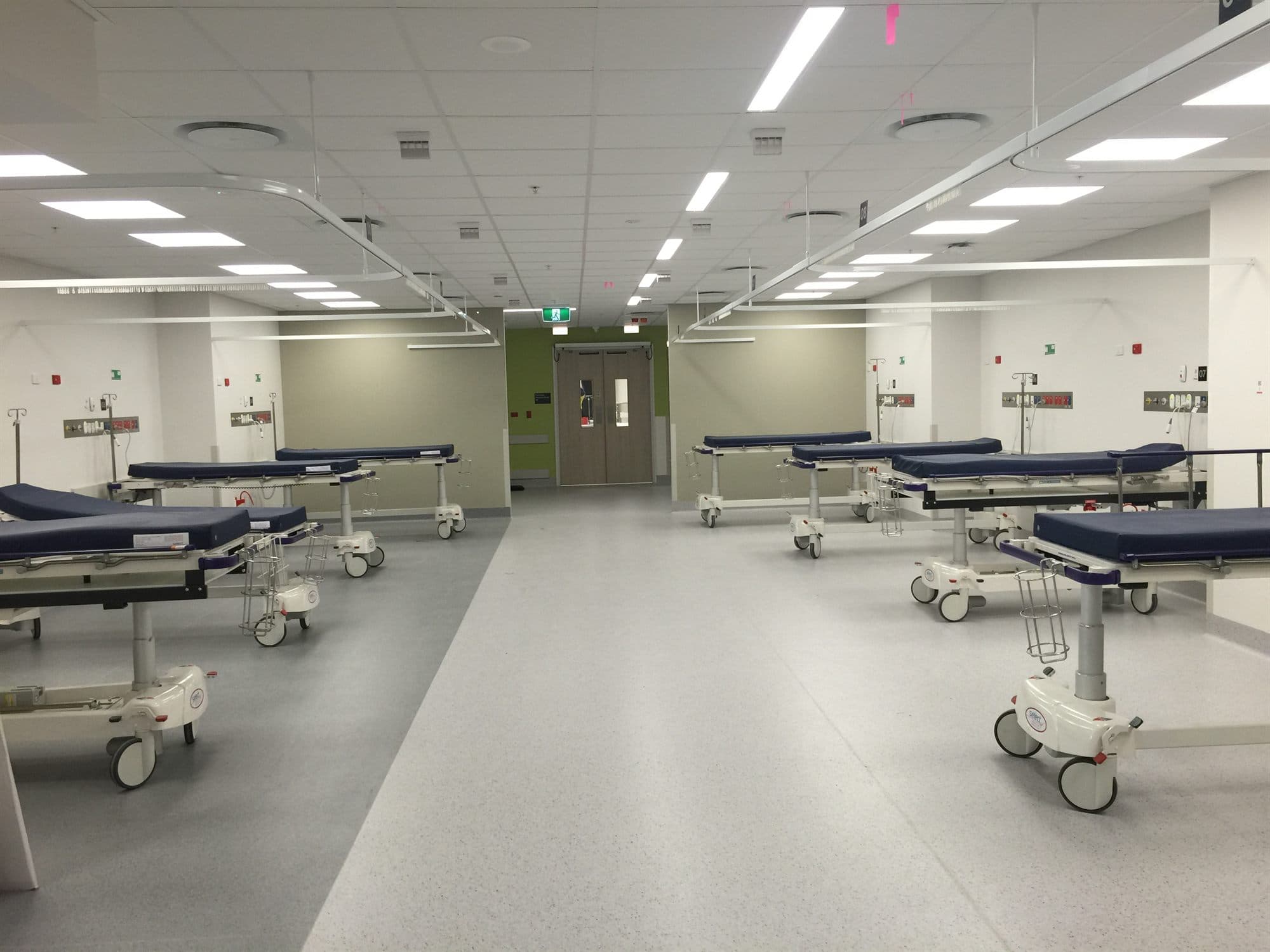An empty recovery bay with rows of patient trolleys, curtain tracks on the ceiling and service panels at each bedhead.